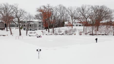 Antenne,-Person,-Die-Schnee-Schaufelt,-Um-Eine-Kleine-Eishockeybahn-Auf-Einem-Teich-Im-Hinterhof-Zu-Schaffen