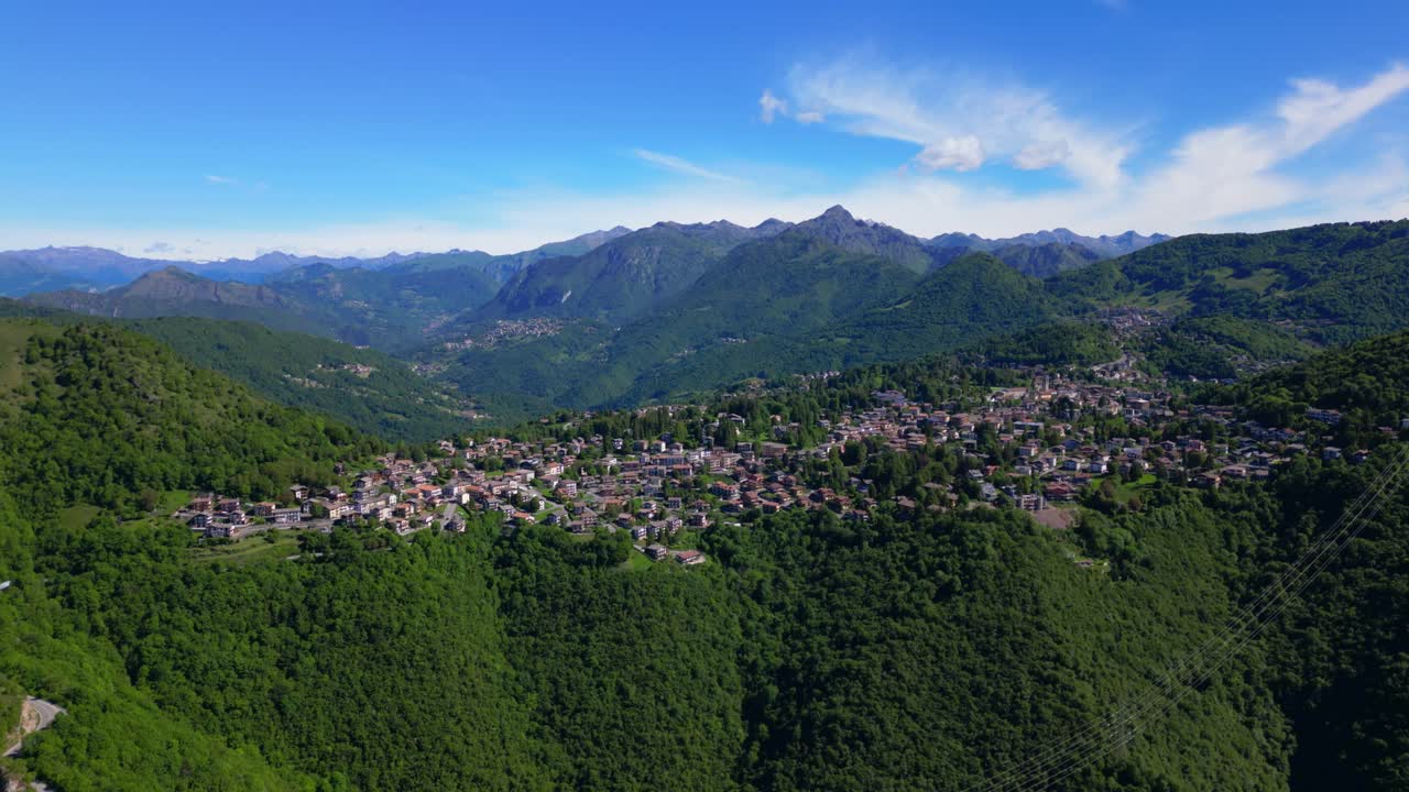 Wide aerial shot of Selvino surrounded by steep green slopes and rugged mountains under blue skies. Shot at Selvino, Italy (Selvino, Italia)
