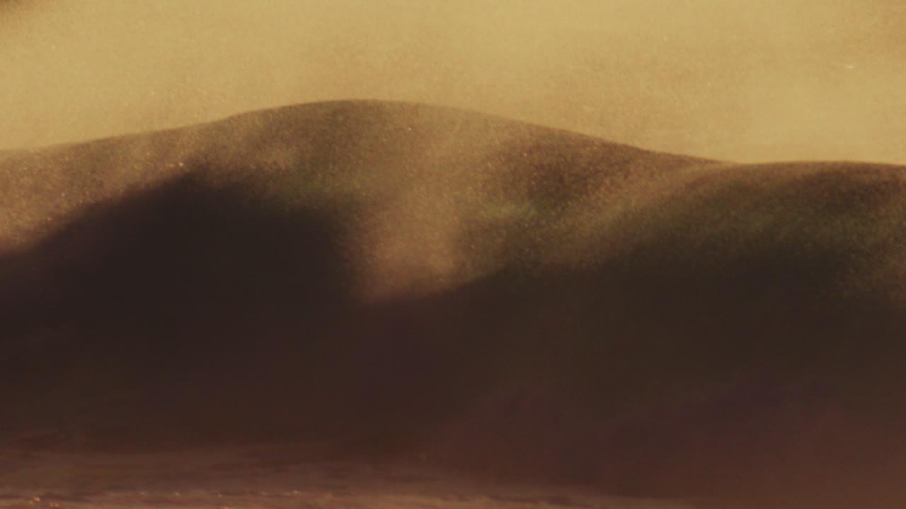 은 물 뒤에 있는 빛의 세부적인 텔레포토 뷰: 부드러운 이른 아침 빛이 파도를 가로질러 춤을 추고, 해안 바람이 바다의 분사 안개를 위로 끌어당기면서.