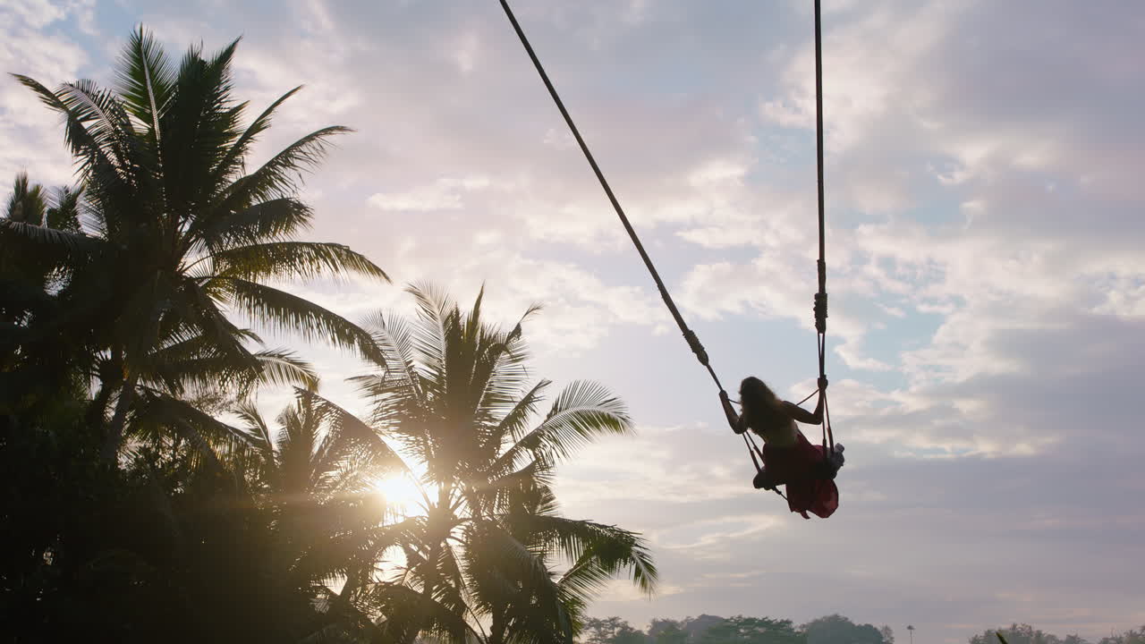 viaggiare donna dondolandosi sulla giungla all'alba godendo di vacanze esotiche seduta sull'altalena con il sole che splende attraverso le palme nella foresta pluviale tropicale vacanza stile di vita libertà