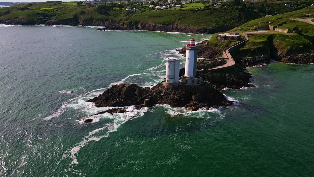 Drone performs a lateral movement above the sea, revealing the Petit Minou lighthouse, stone path, crashing waves, cliffs and surrounding vegetation - Brittany in France