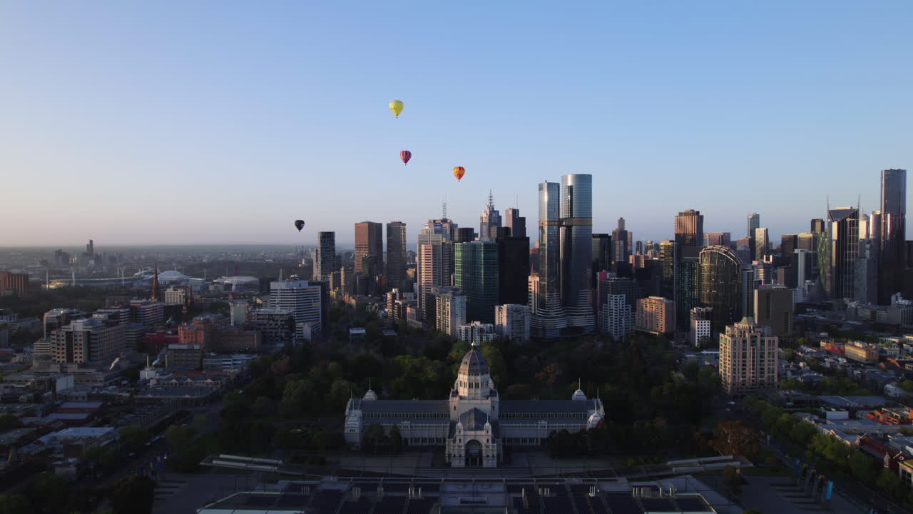 Aerial view backwards over the Carlton Gardens with Hot-air balloons above the Melbourne skyline