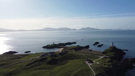 aerial view circling idyllic ynys llanddwyn island with hazy snowdonia mountain range across shimmering irish sea at sunrise