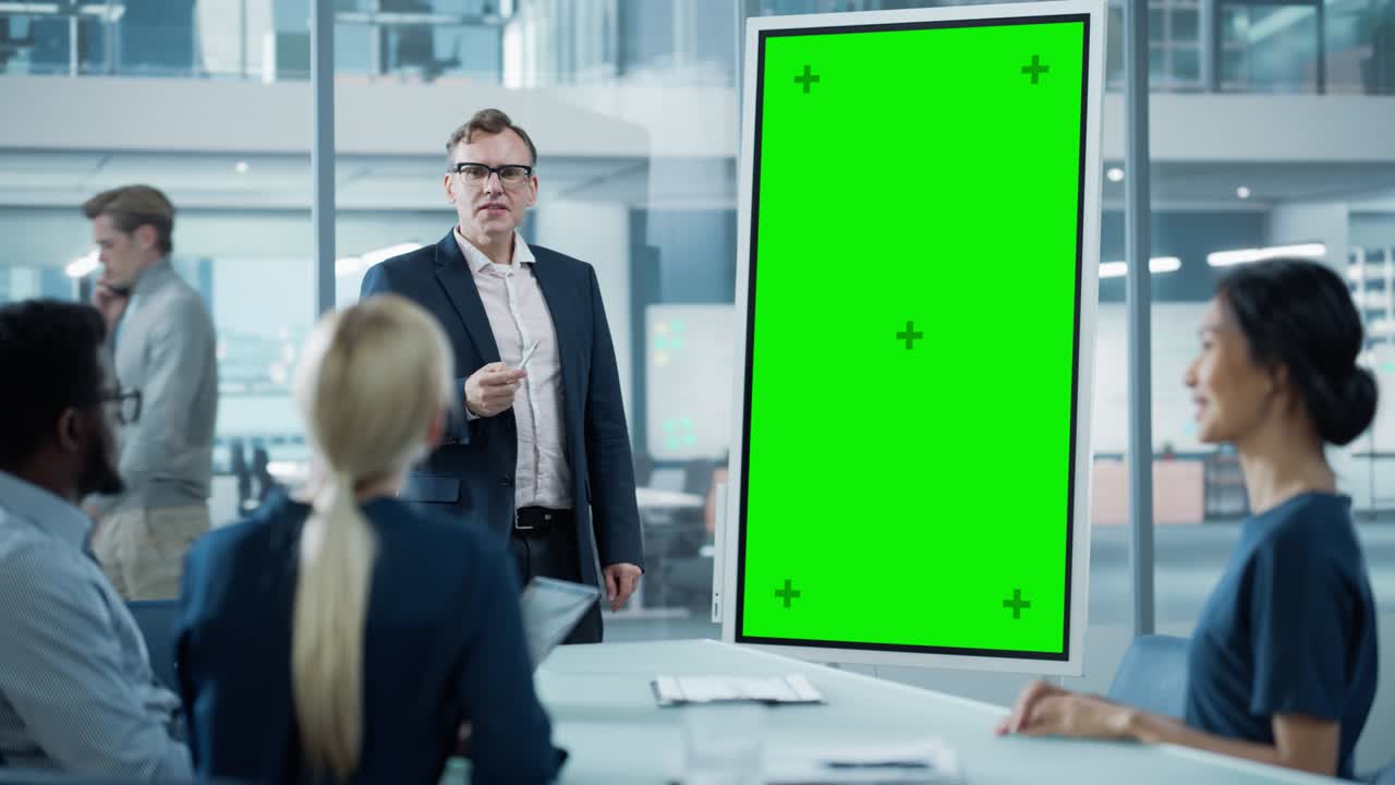 el gerente de operaciones de la compañía realiza una presentación de la reunión para un equipo de economistas. hombre adulto utiliza pizarra digital con pantalla verde vertical para mostrar la maqueta. la gente trabaja en una oficina de negocios.