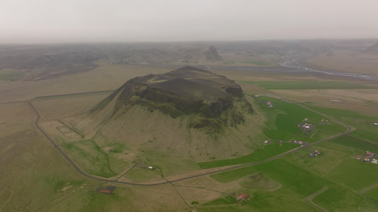 Aerial view of Petursey mountain in Iceland, surrounded by vast fields and rural landscapes, under a misty sky, with small farms nearby.