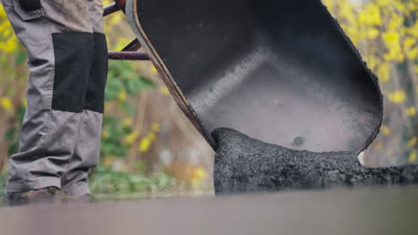 construction worker off-loading hot asphalt tarmac mixture from wheelbarrow during pavement repairing work