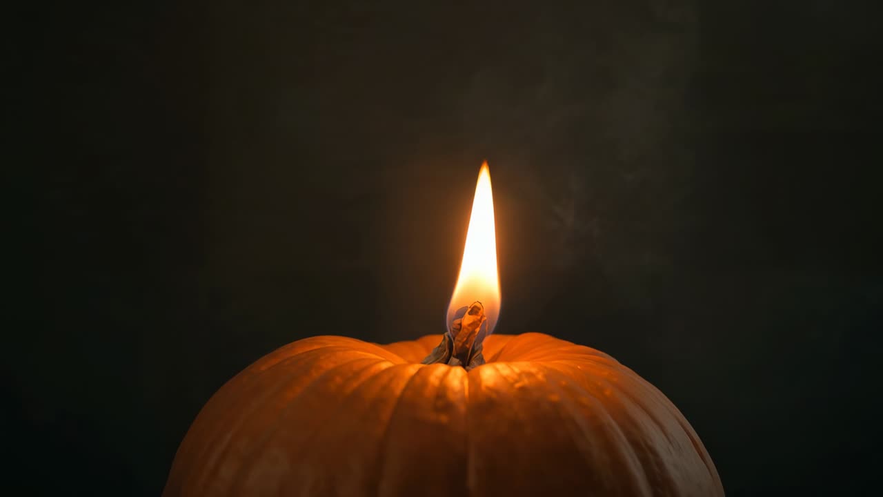 Fiamma tremolante da stoppino acceso nella zucca, che illumina le creste e il fumo che si arriccia nell'interno scuro