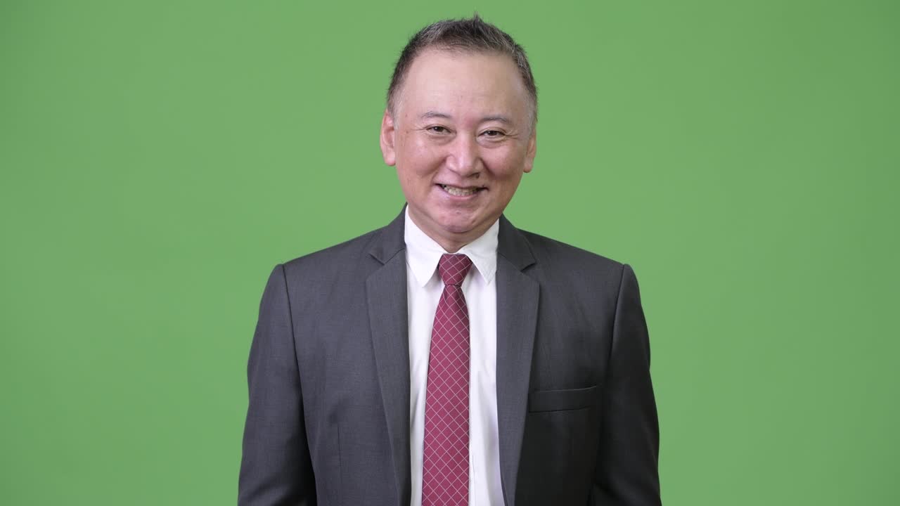 성숙한 행복한 일본 사업가 녹색 배경에 미소 짓고