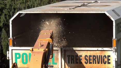 medium shot of wood chips expelled from chute of wood chipper into the back of a truck in slow motion