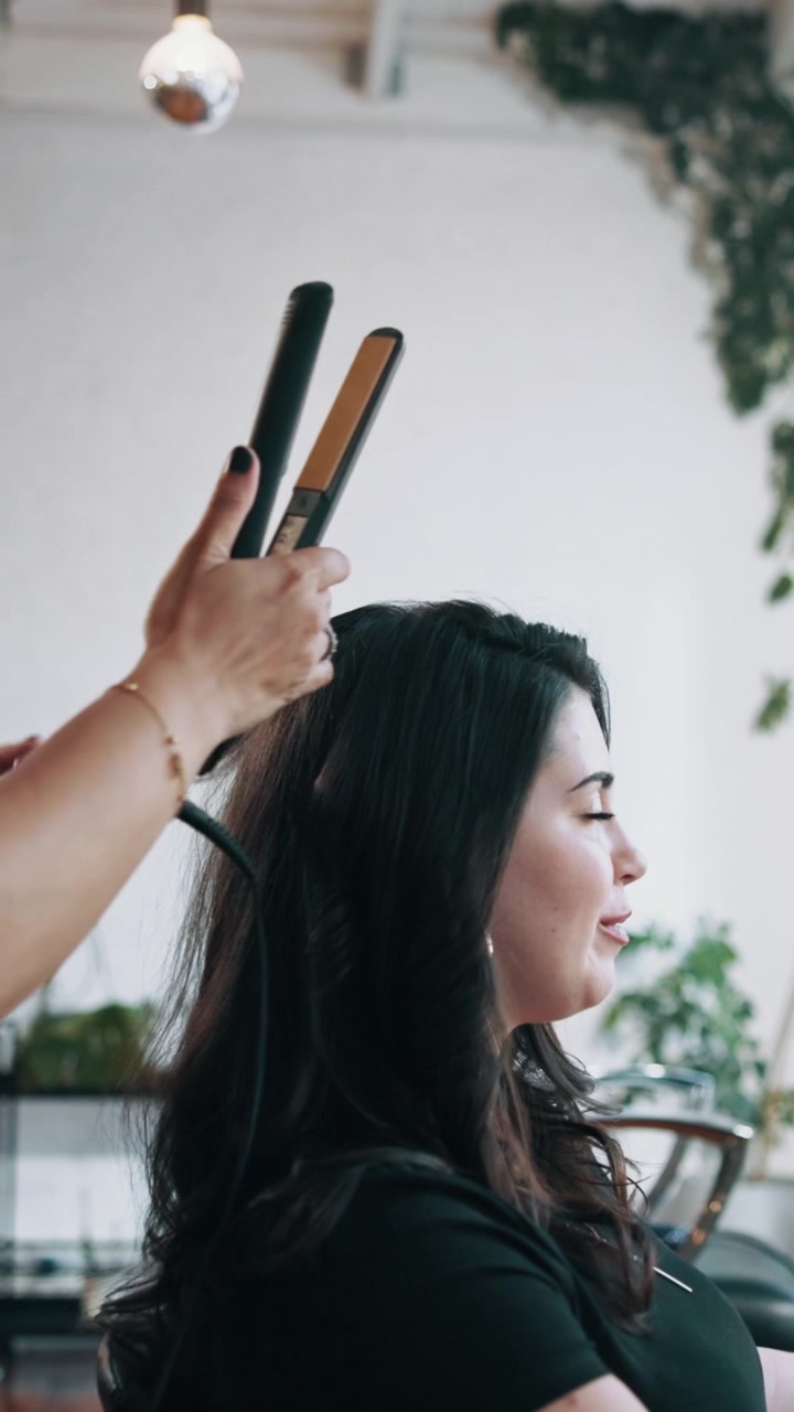 Parrucchiere che liscia i capelli di una cliente in un salone