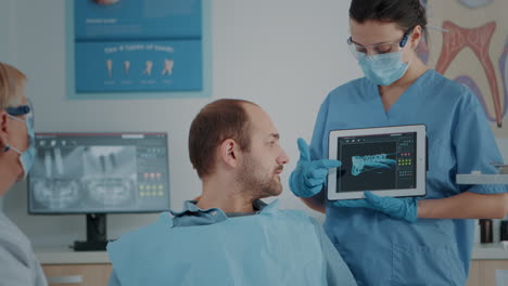 asistente de odontología mostrando los resultados de la exploración de rayos x en la tableta al paciente