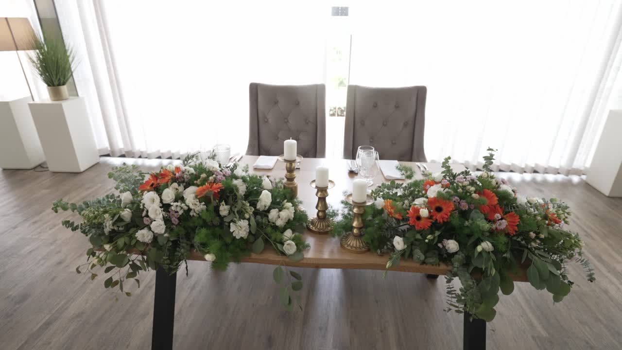 Tavolo degli sposi elegantemente decorato con lussureggianti composizioni floreali e accenti di candele.