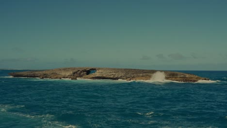 las olas del pacífico persiguen la orilla de esta isla rocosa y desierta con su propio puente de piedra natural creado por años de erosión en hawai.