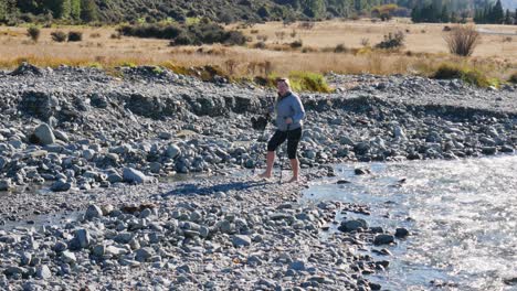 hiker crosses mountain stream barefoot while holding boots