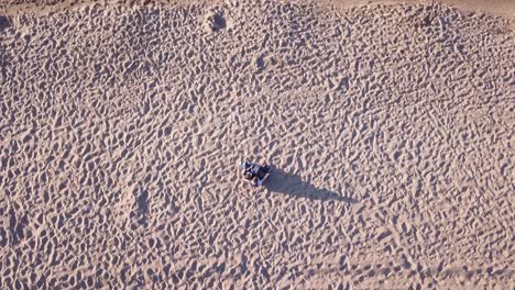 Toma-Aérea-De-Una-Pareja-Joven-Sentada-En-La-Playa-De-Arena,-Abrazándose