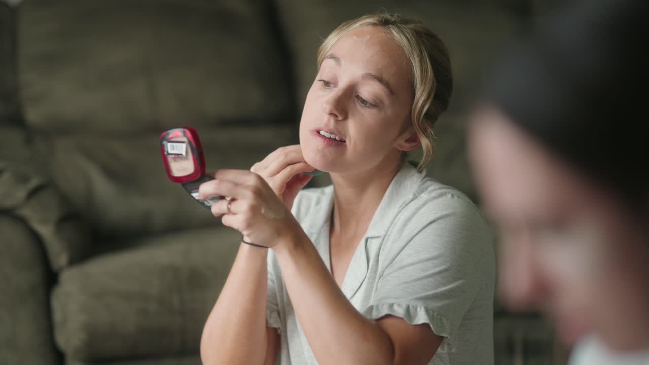una mujer joven aplica maquillaje con una licuadora de belleza junto a la ventana.
