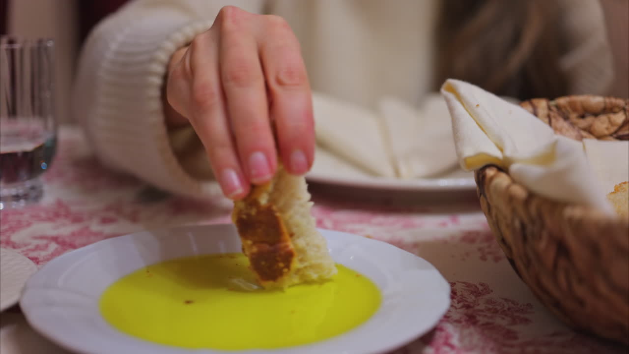 Close up of a woman dipping bread in olive oil and eating it at a restaurant