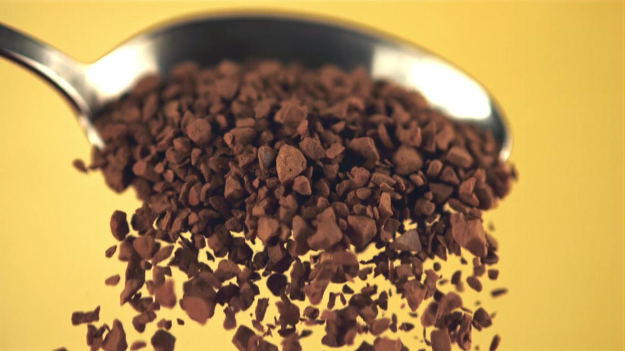 Gránulos de café instantáneo cayendo de una cuchara en cámara superlenta