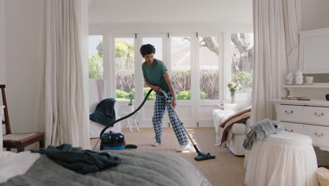 happy young man dancing with vacuum cleaner at home cleaning bedroom celebrating success having fun dance in on weekend morning feeling positive