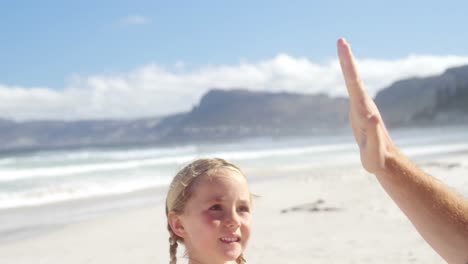 father and daughter giving high five to each other at beach