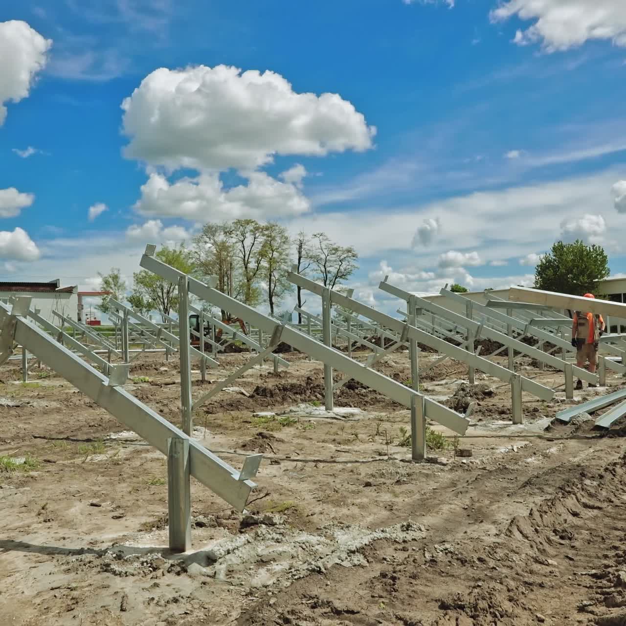 Construction of solar farm on the ground. Workers in uniform and orange helmets build metal basis for solar panels. Time lapse.