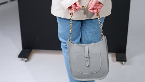 beautiful grey leather bag with golden chain handle in female hands. woman in jacket and jeans holding a modern handbag.