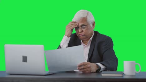 Tensed-Indian-senior-manager-reading-business-reports-Green-screen