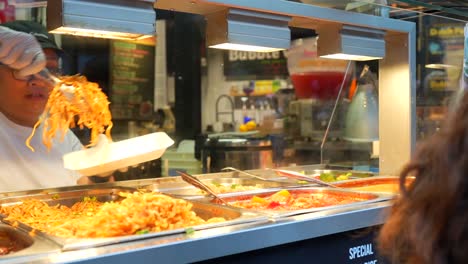 Asian woman serving noodles to customer at Camden Town street food market in London