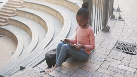 sitting on steps, african american girl using tablet for studying outside school building