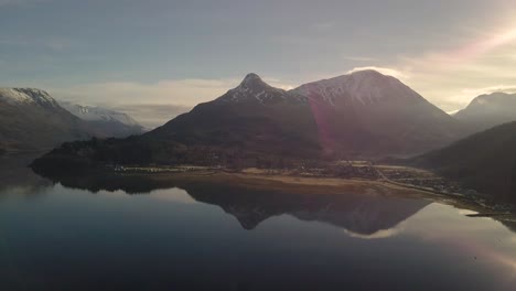 Schwenk-Drohnenaufnahme,-Die-Die-Wunderschöne-Bergkette-Schottlands-Mit-Schneebedecktem-Berggipfel-An-Einem-Sonnigen-Tag-Zeigt---Seespiegelung-Der-Berge-Auf-Der-Wasseroberfläche