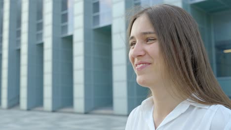 Smiling-woman-talking-with-someone-while-standing-in-front-of-grey-building,-side-view