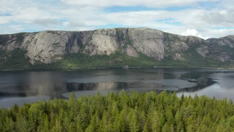 aerial past a forest along the nisser lake with the langfjell mountain range in the background, treungen, telemark, norway