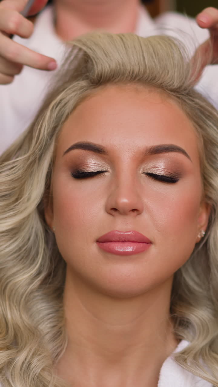 Attractive young woman with glamorous makeup sits undergoing hairstyle made with professional hairdresser in beauty salon closeup slow motion