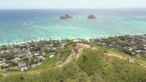 hikers on mountain range overlooking ocean on tropical island with land emerging from the ocean blue water along the coast