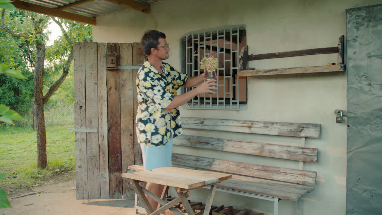 Man decorating a wooden shelf with flowers on a porch