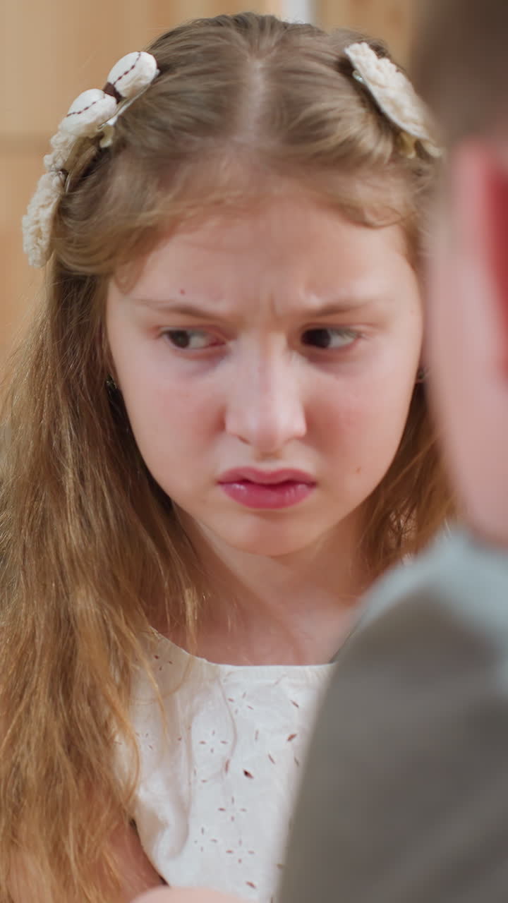 primo piano di una giovane ragazza bianca accigliata mentre viene rimproverata in cucina, che mostra la reazione di una figlia preadolescente al rimprovero dei genitori, mani che giocherellano con le luci decorative, atmosfera tesa ed emozione cruda in tutte le immagini