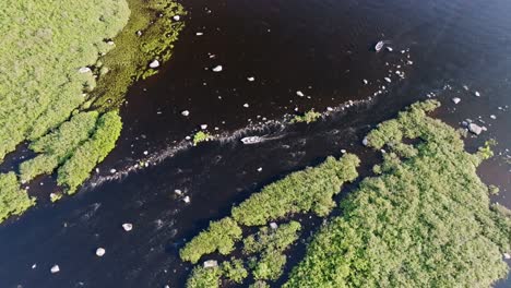 top-down aerial shot of boat navigating stream outlet in remote canadian lake