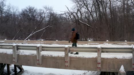 Steady-shot-of-a-man-walking-across-a-bridge-in-a-rural-forest-area