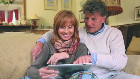 mature couple sitting on the couch using their tablet pc