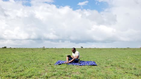 time lapse shot of a black man who sits on a blanket in the grass taking notes in a book