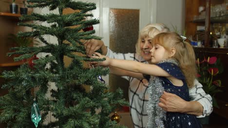 Children-girl-with-grandparents-couple-decorating-artificial-Christmas-pine-tree-at-old-fashion-home