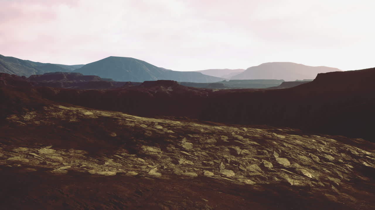 Vast volcanic landscape with distant mountains under hazy sky at sunset