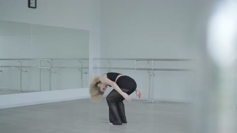 chica en forma con ropa negra actuando contemporáneamente. bailarina muestra movimientos fluidos, cuerpo y manos ondas en la habitación blanca. coreografía de danza de ballet moderno. joven se mueve suavemente