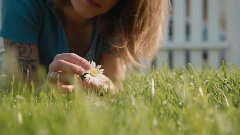 woman lying in grass examining a daisy