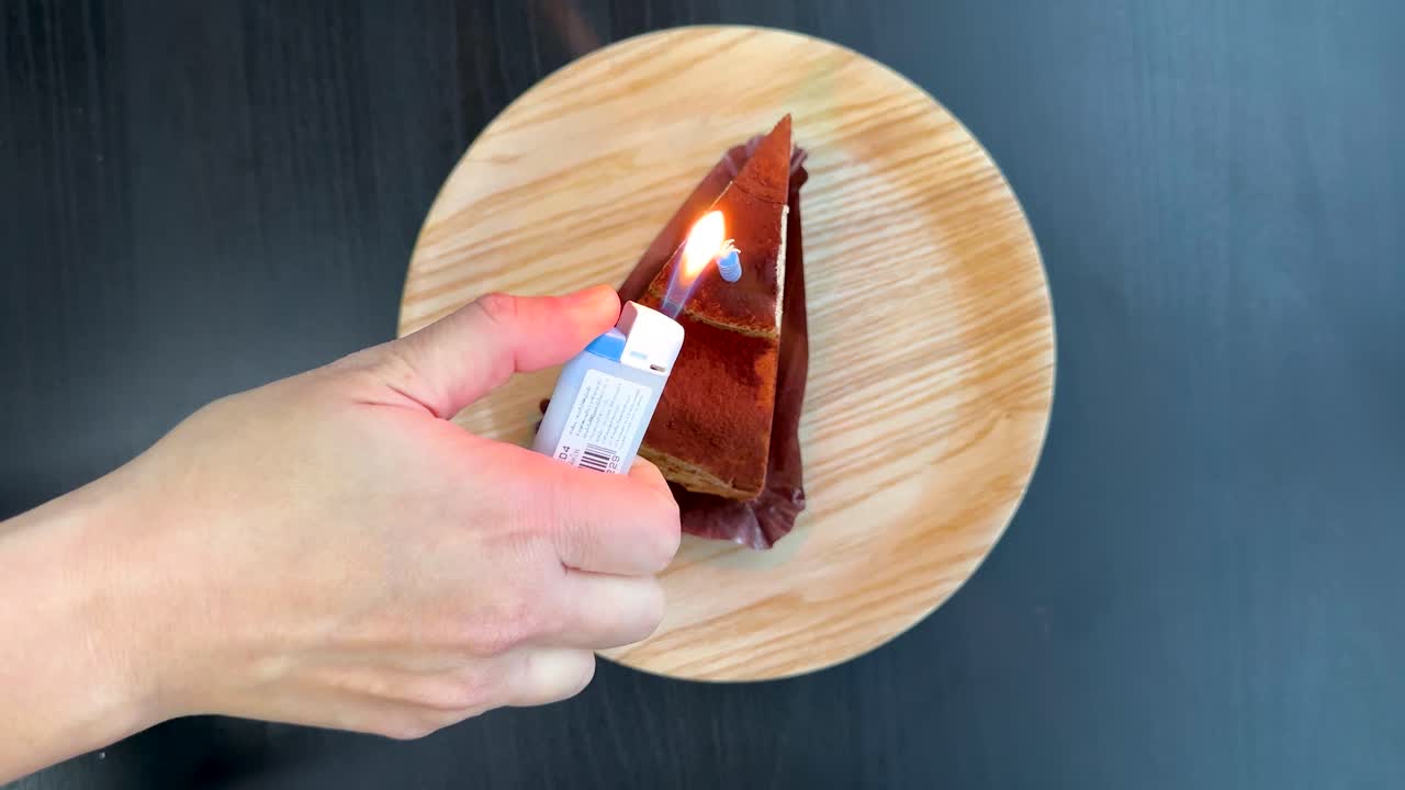 Hand places and lights a small candle on tiramisu cake slice under bright, even lighting