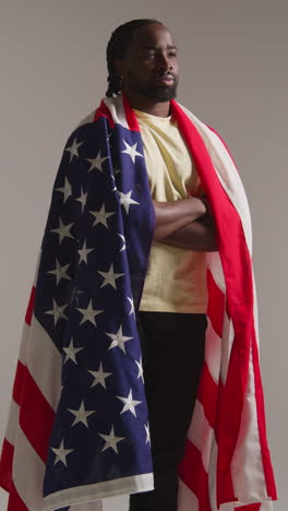 vertical video studio shot of man wrapped in american flag celebrating 4th july independence day