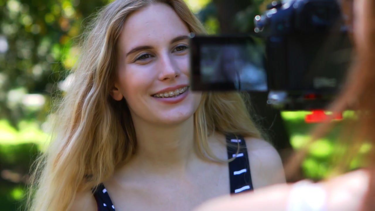 Ung kvinna i parken gör en vlogg för att dela med sin publik på sociala medier. Spelar in en blogg med kamera
