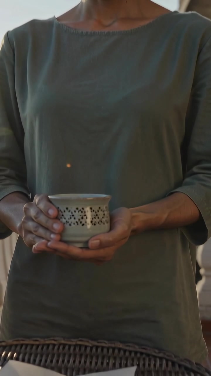 Vertical video: Lowering woman in olive tunic looking down placing cup on balcony table by booklet