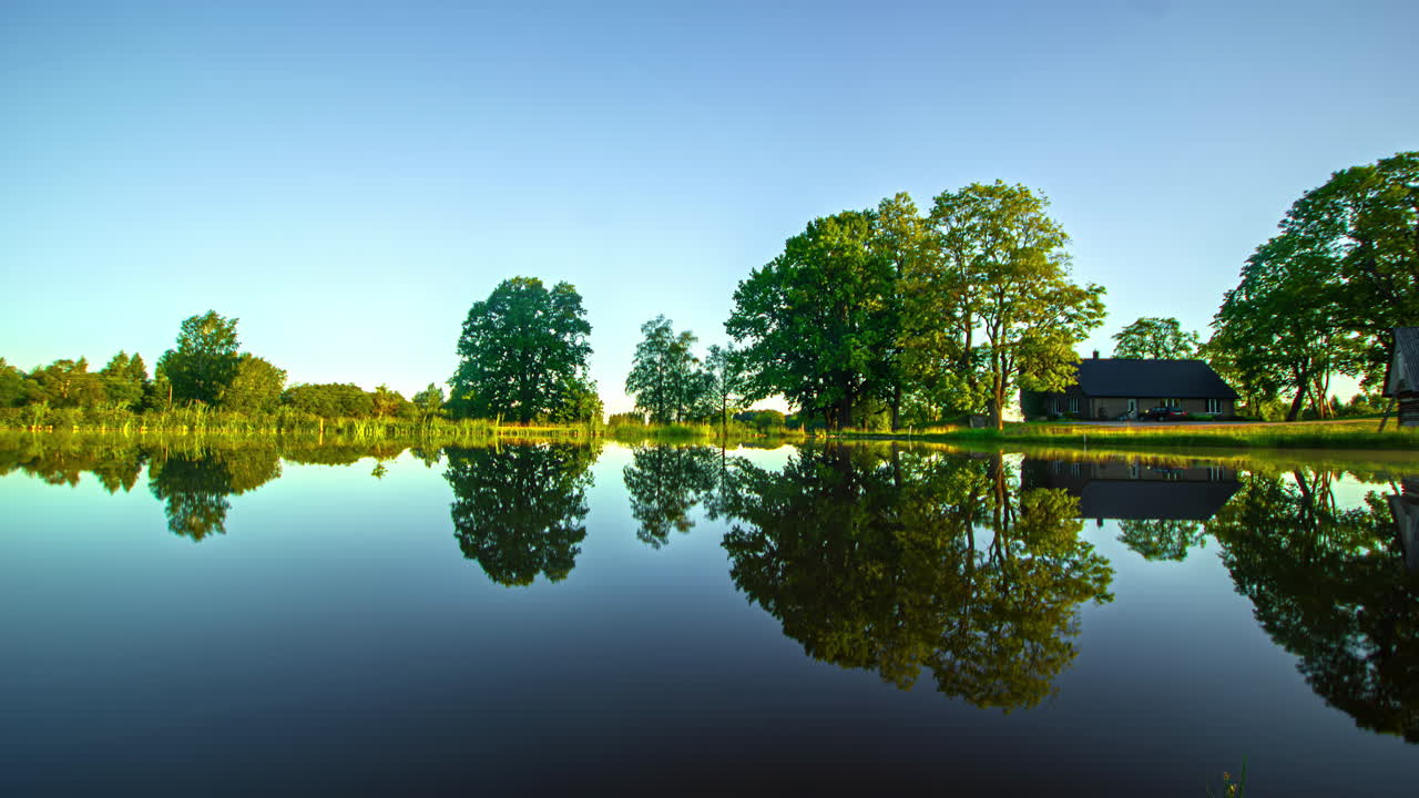Timelapse captures the beauty of a rural landscape with a tranquil lake and house as it transitions through the four seasons with snow, autumn leaves and frozen lake