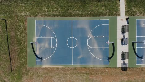 una toma estática aérea de arriba hacia abajo de una cancha de baloncesto azul al aire libre durante el mediodía con largas sombras de proyección 4k